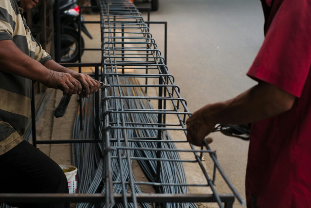 Workers manually assembling steel rebars for a construction project in an Indonesian setting.